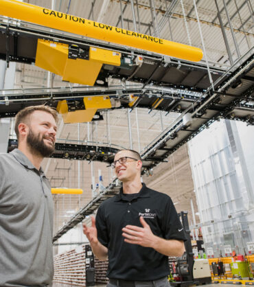 BastianSolutions_20191003-Parts_Town_Case_Study-DSC_7737 ACT-consultation-for-facility-improvements-two-associates-speaking-in-a-warehouse