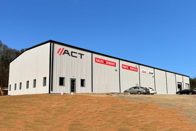Industrial warehouse with white metal siding, red banners for Sales, Service, Parts, Rentals, and cars parked outside on a sunny day
